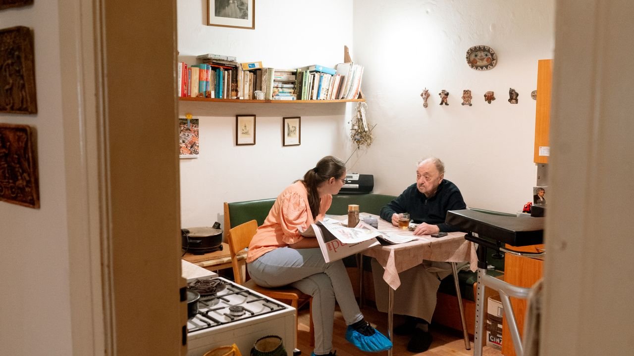 A caregiver and an older woman sitting together at a table in her home