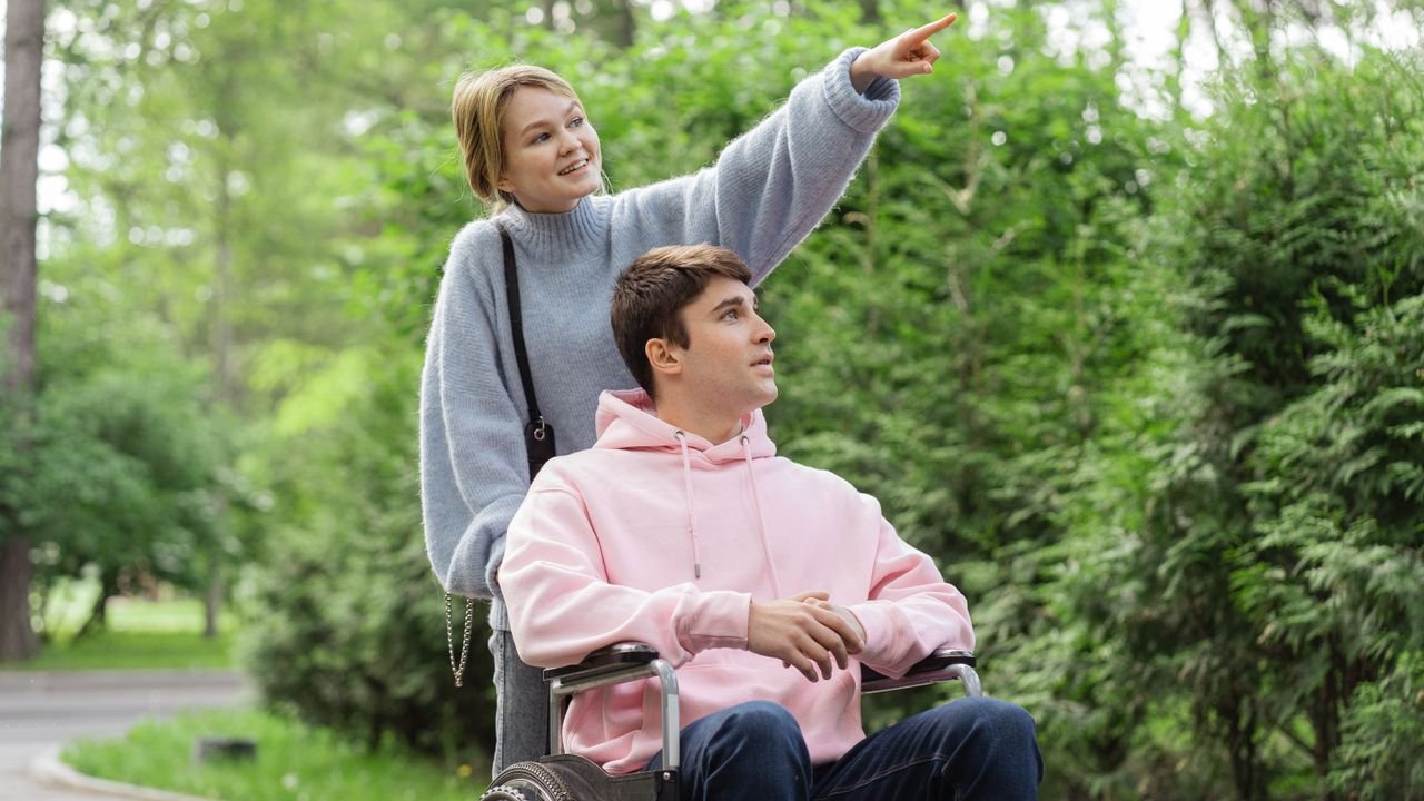 A support worker and a young man in a wheelchair enjoying a walk among the trees