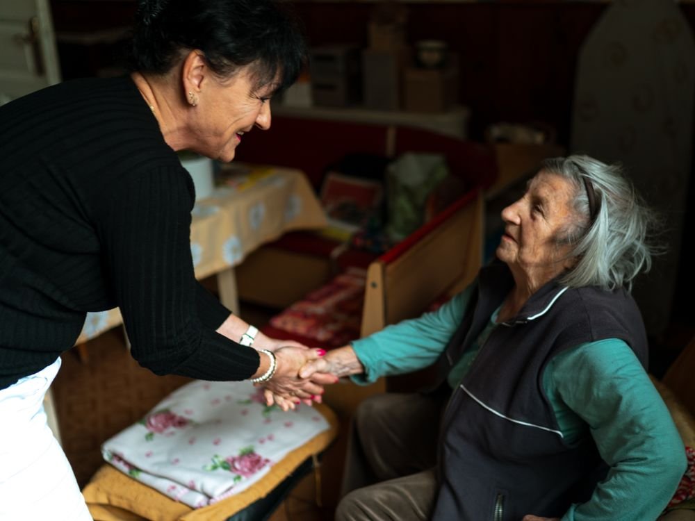 A caregiver greeting an older woman warmly in her own living room