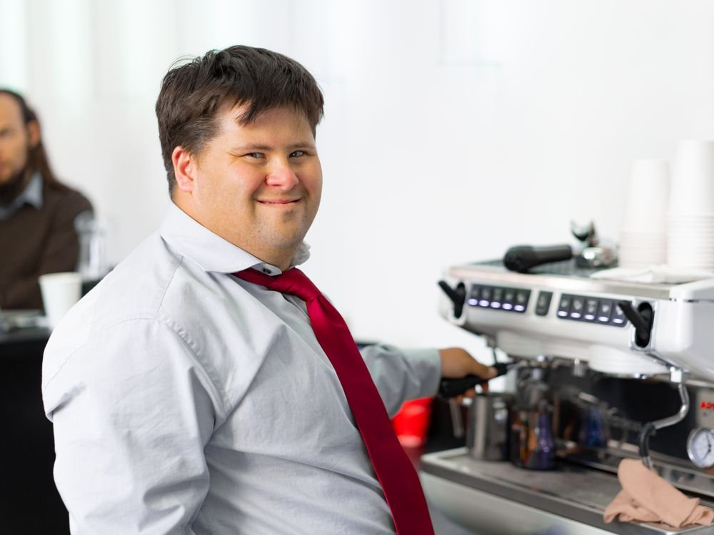 A young man with Down syndrome working confidently behind a cafe coffee machine