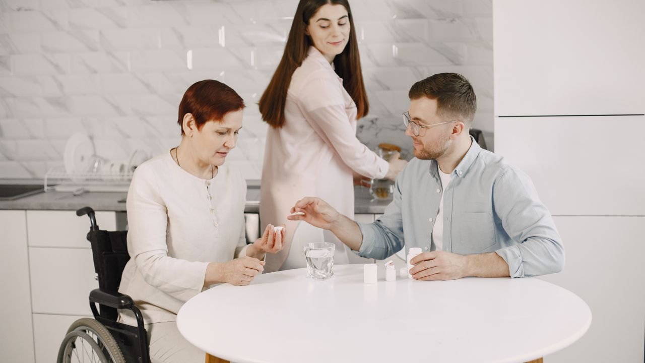 A caregiver helping a woman in a wheelchair with her medication at the kitchen table
