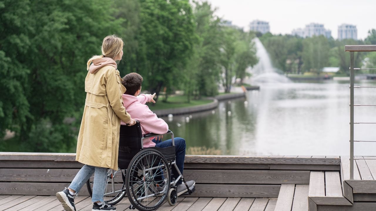 A caregiver walking with a client in a wheelchair along a lakeside path