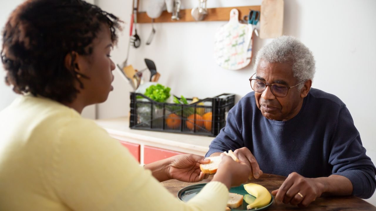 A caregiver helping an older man with a meal in his own kitchen