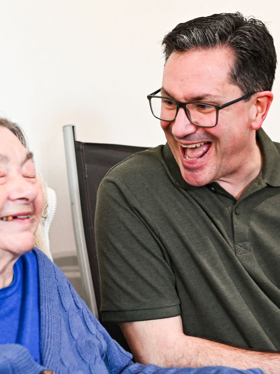 A caregiver and an older woman laughing together indoors