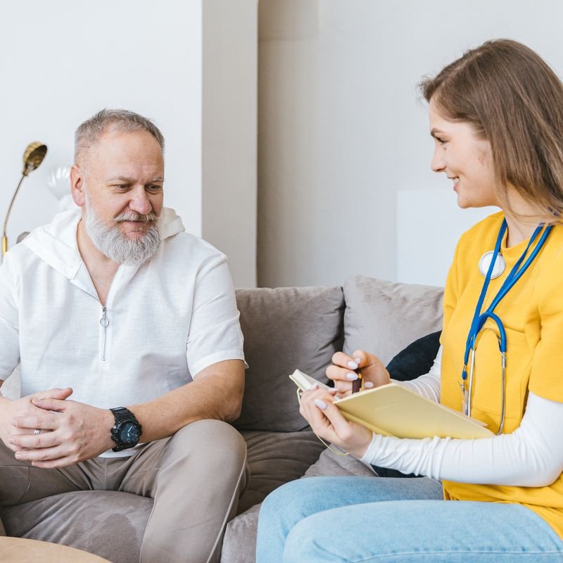 A care professional talking with an older man on his sofa